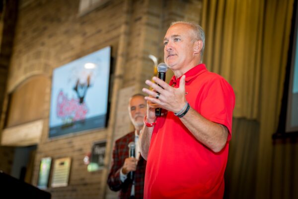 A speaker in a red polo addresses the room during the Kick-Off Lunch