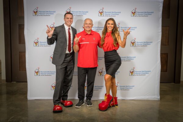 Three attendees in Texas Tech red raise guns up in front of the Ronald McDonald House Southwest banner