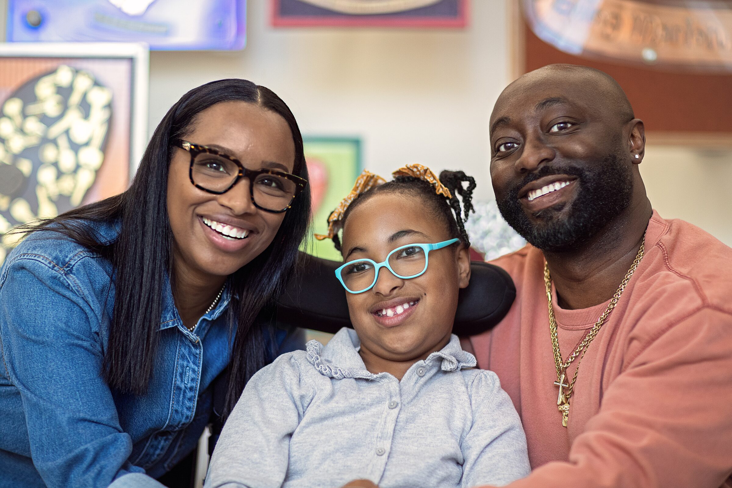 A smiling family of three sitting together in front of a colorful wall